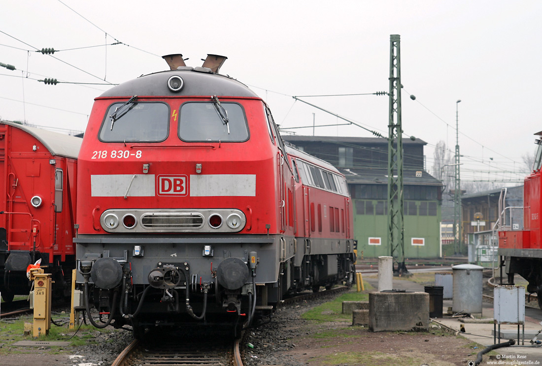 Abschlepplokomotive 218 830 in verkehrsrot mit Lokschuppen in Köln Betriebsbahnhof