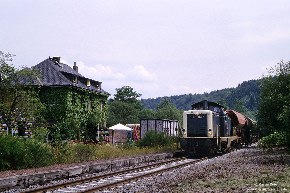 212 328 mit Schotterzug im Bahnhof Scherl mit Empfangsgebäude