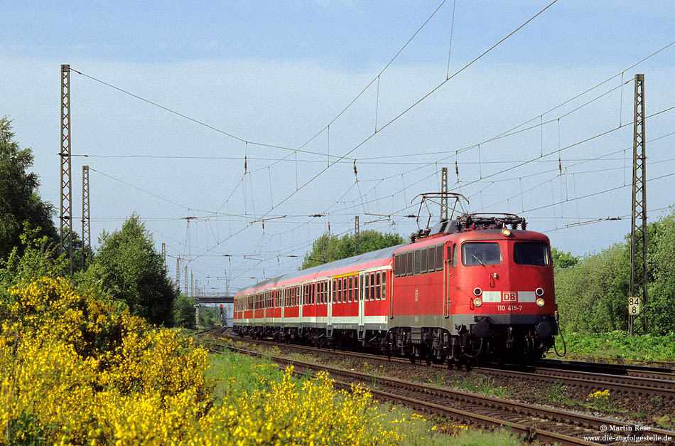 110 415 in verkehrsrot mit RB nach Osnabrück im Bahnhof Ostbevern mit blühendem Ginster