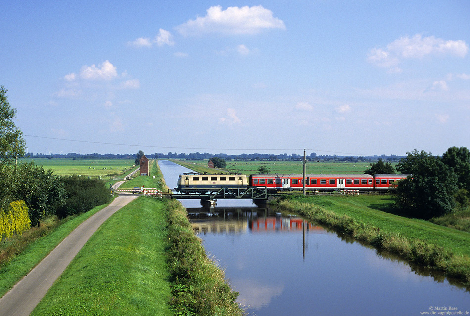 Über Jahre hin prägte die Baureihe 141 das Bild des Nahverkehrs auf den elektrifizierten Strecken im Weser-Ems-Gebiert. Am 5.9.2002 überquert der RE24539 (Emden – Oldenburg) bei Stickhausen Velde den Nord-Georgsfehner-Kanal.
