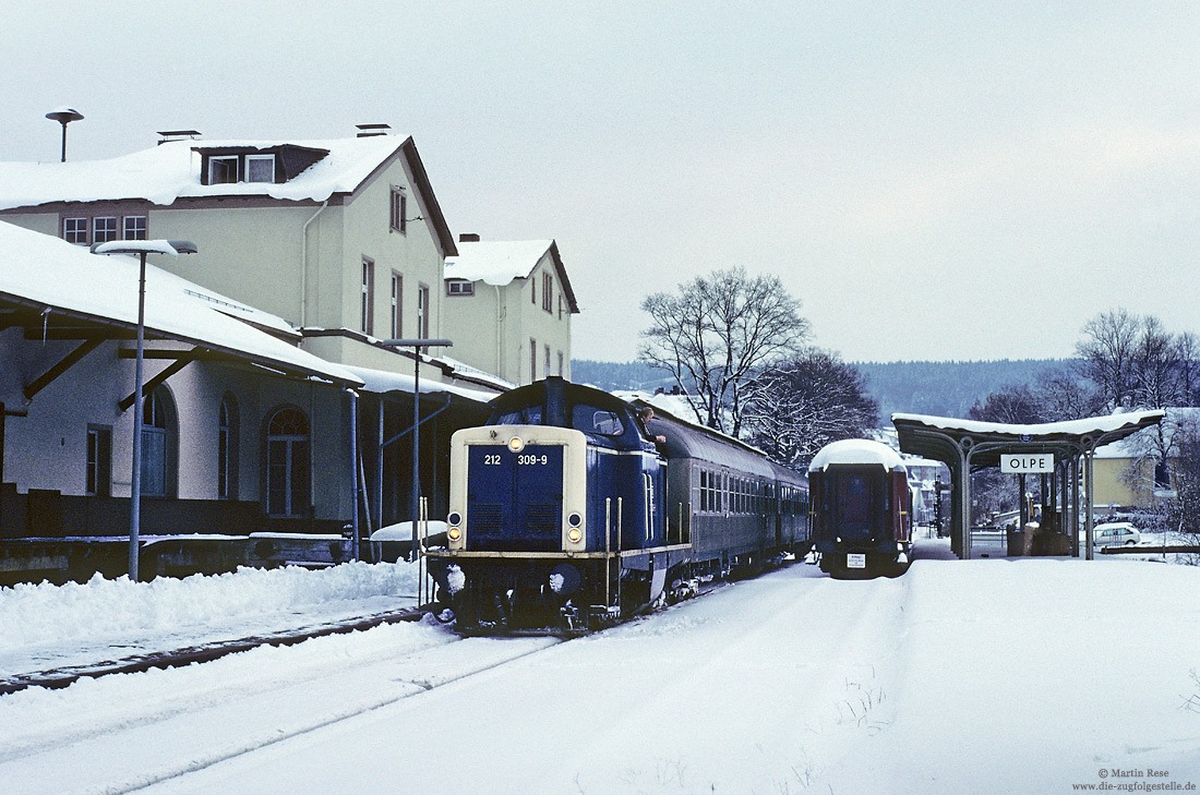 212 309 in ozeanblau beige mit Nahverkehrszug im Bahnhof Olpe mit Bahnhofsgebäude im Schnee